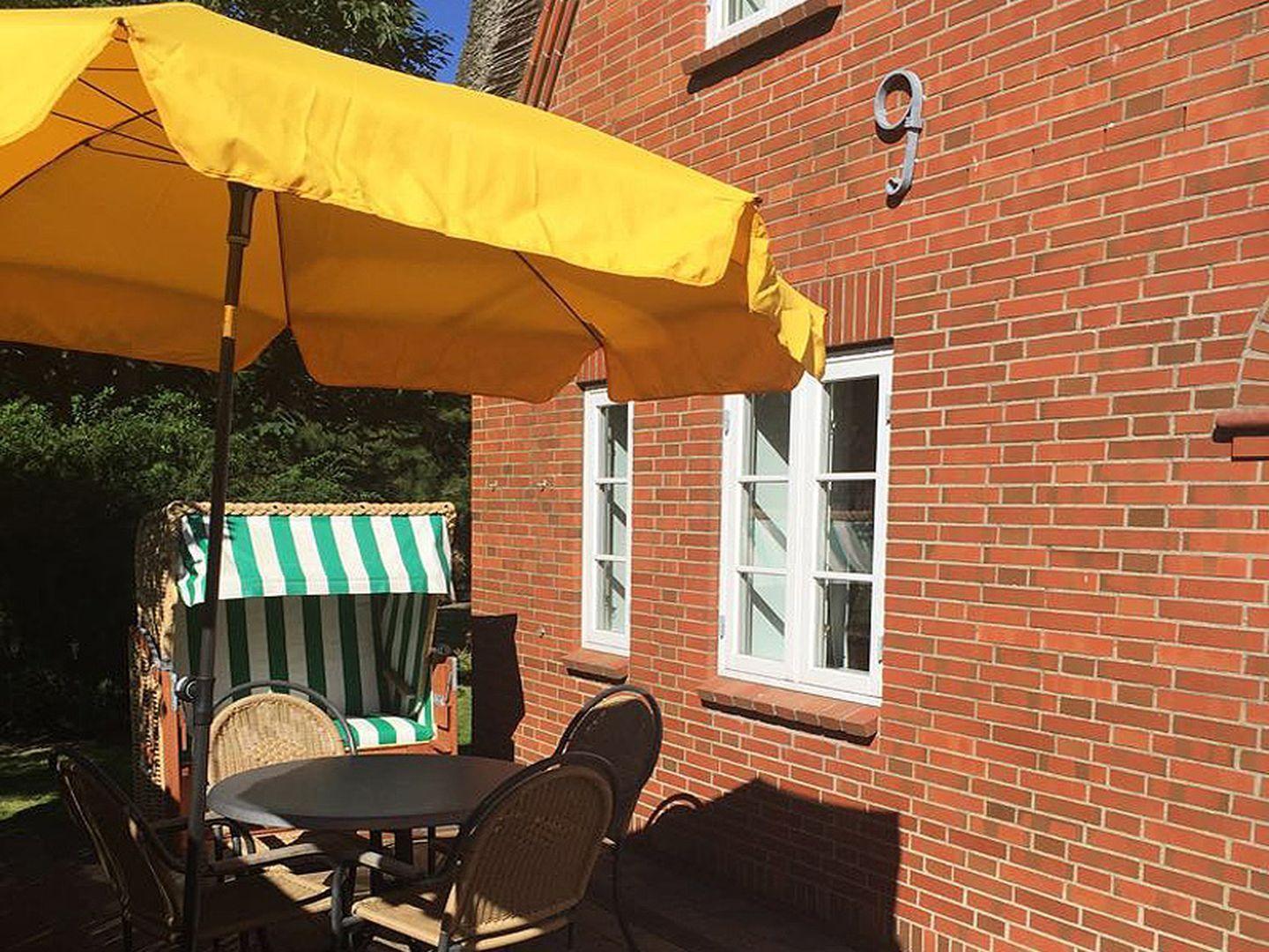 Roter Backsteinbau mit Terrasse, gelber Sonnenschirm und grün-weißem Liegestuhl.