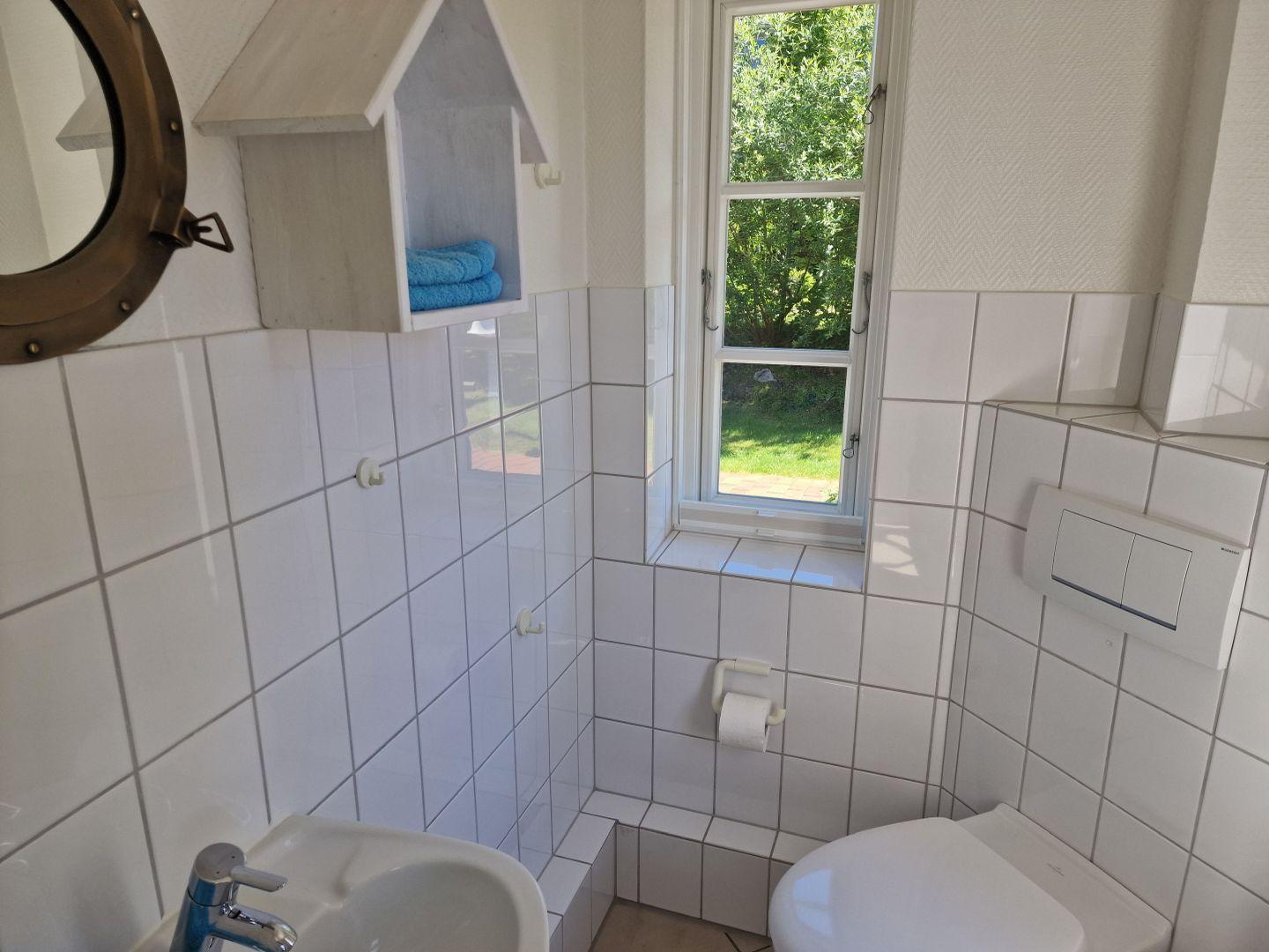 Badezimmer mit Toilette, Waschbecken und Fenster mit Blick auf Garten