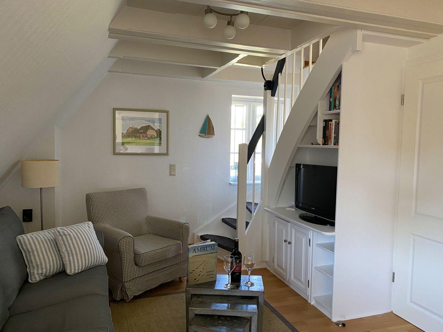 Wohnzimmer mit Sofa, Sessel, Fernseher und Treppe.