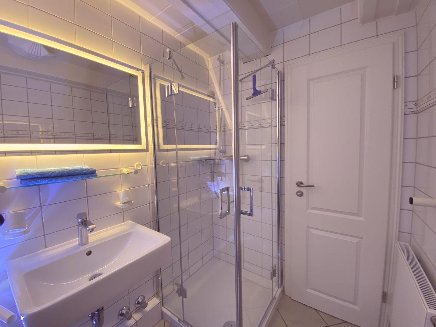 Badezimmer mit Dusche, Waschbecken und beleuchtetem Spiegel