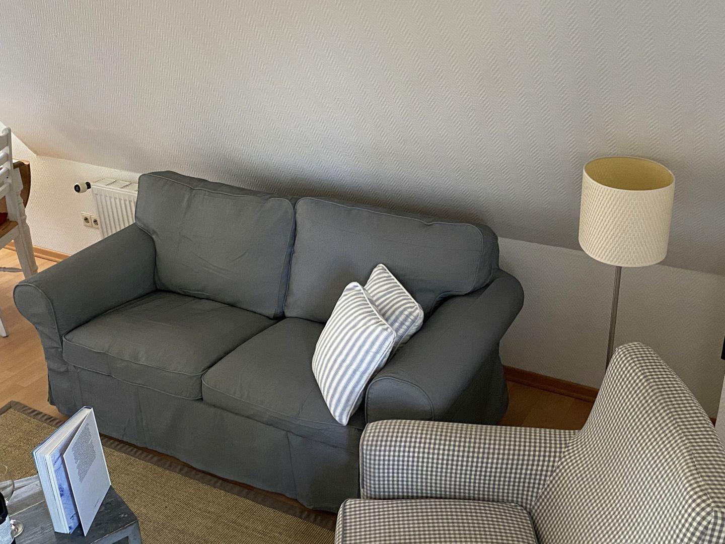 Grauer Sofa mit gestreiften Kissen, Stehlampe und Holzboden.