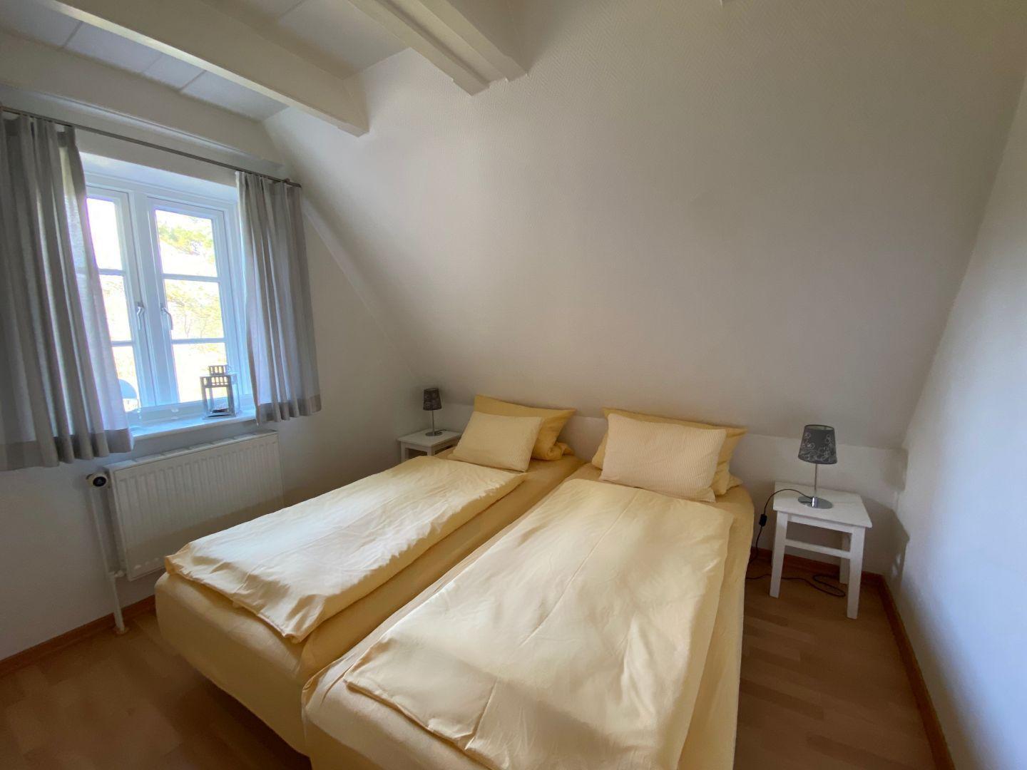 Zimmer mit zwei Betten, Fenster und Nachttischen.