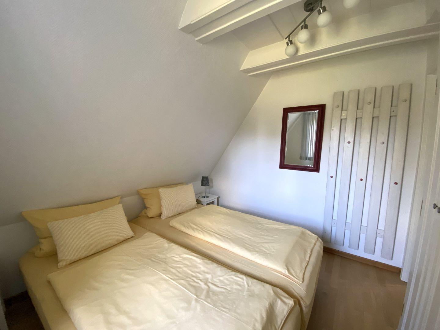 Schlafzimmer mit Doppelbett, Spiegel und Heizkörper an der Wand.
