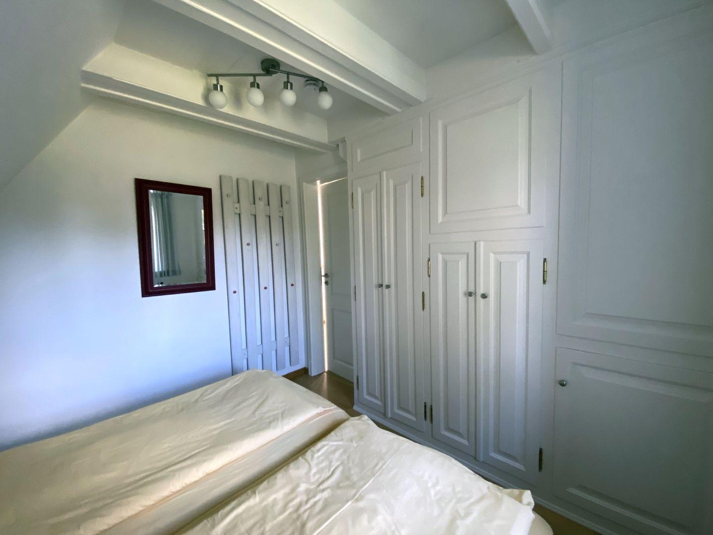 Schlafzimmer mit Bett, weißen Schränken und Spiegel an der Wand.