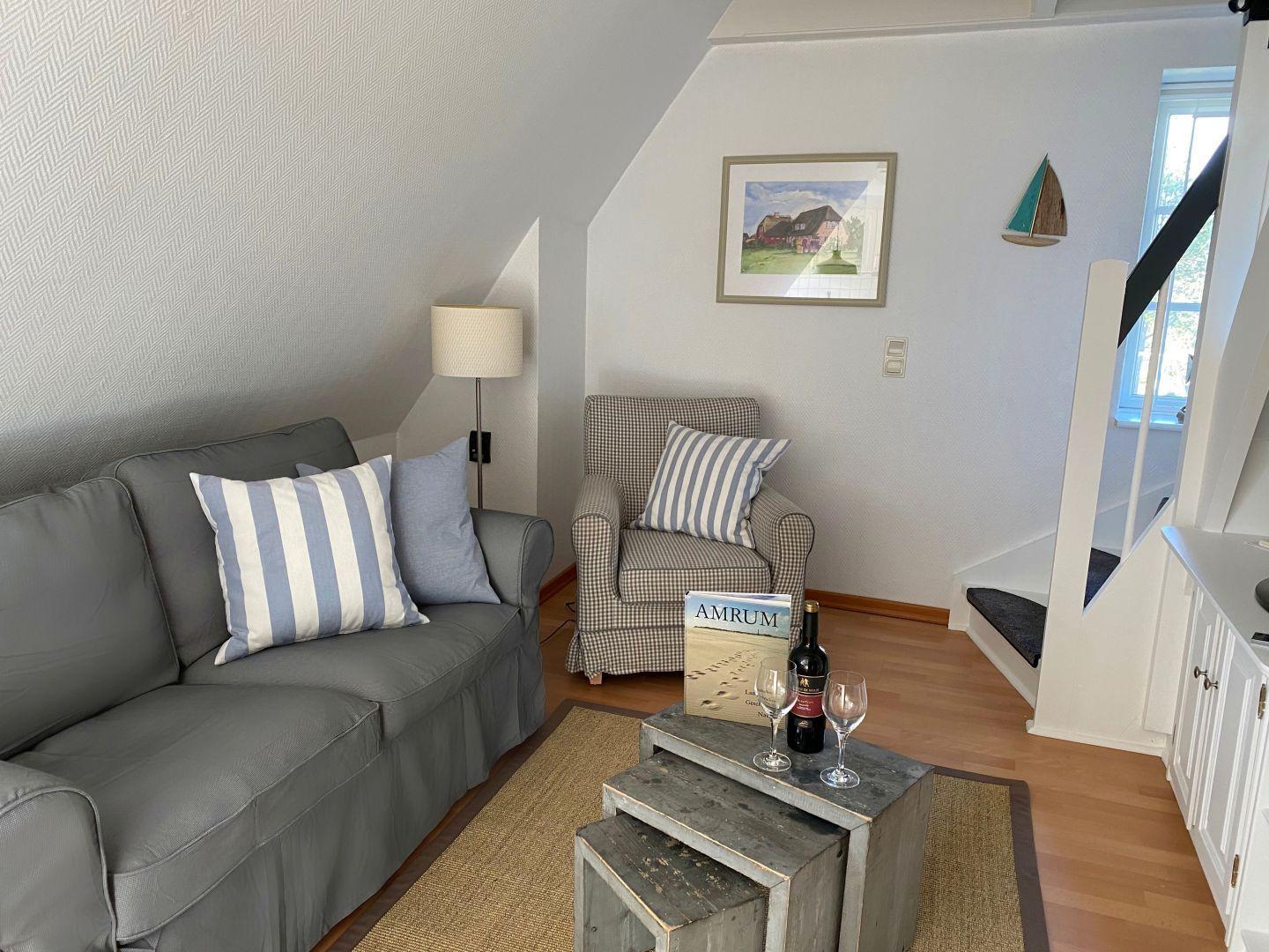 Wohnbereich mit Sofa, Sessel und Tisch. Wandbild und Segelboot-Dekoration.