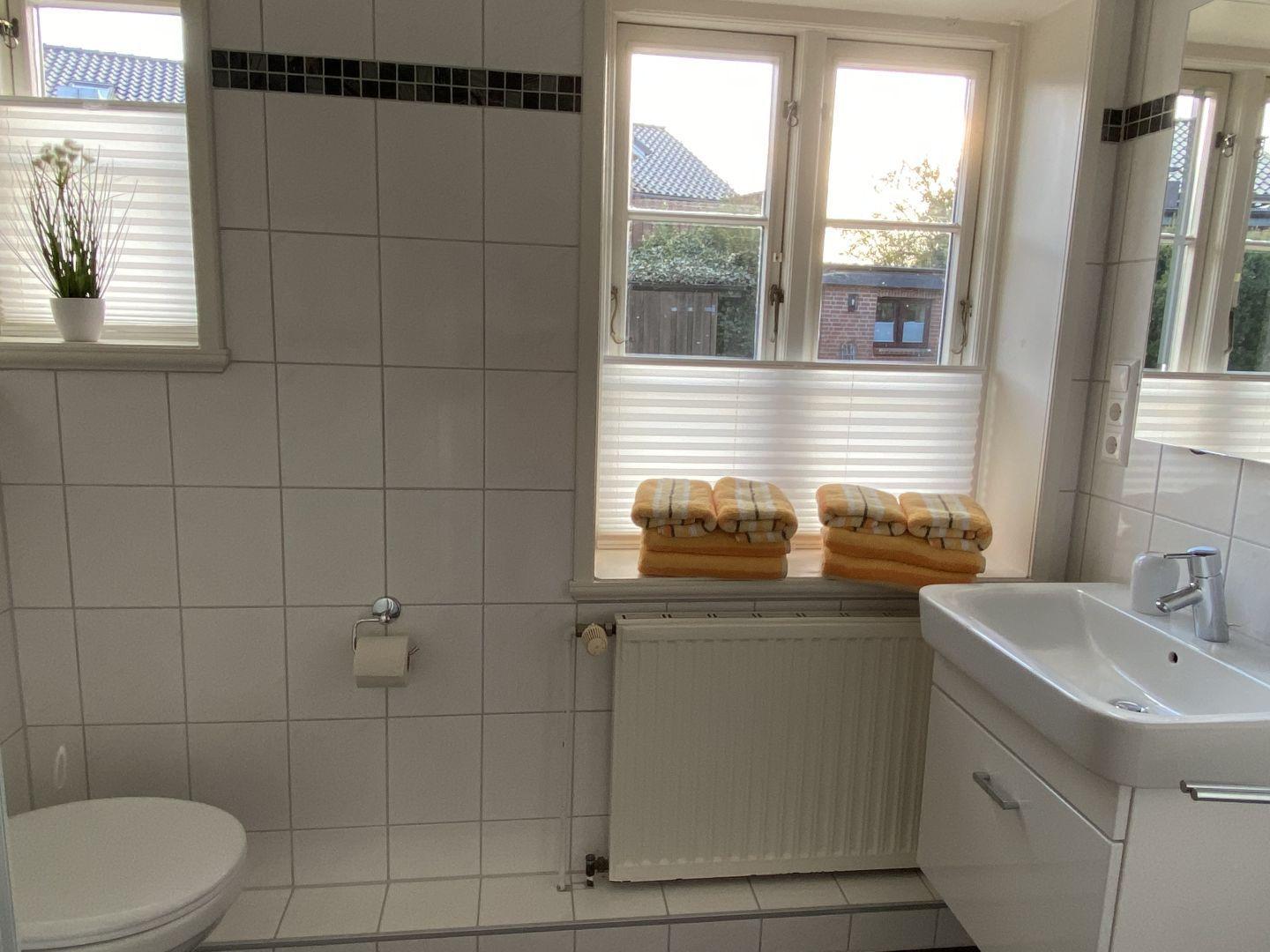 Badezimmer mit Toilette, Waschbecken und Fenster mit Handtüchern.