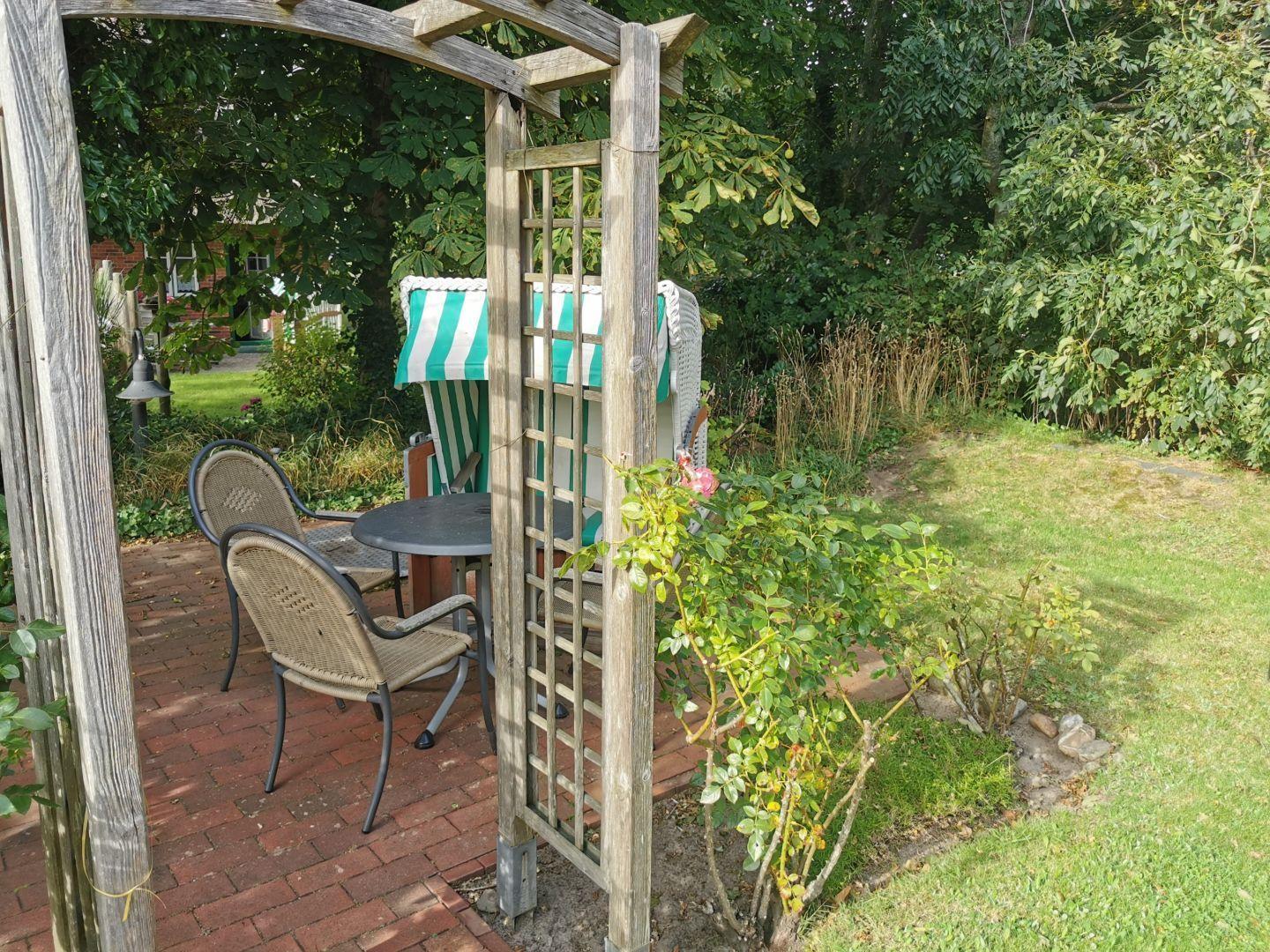Gartenbereich mit Holzarkade, Tisch, Stühlen und grün-weißem Sonnenschirm.