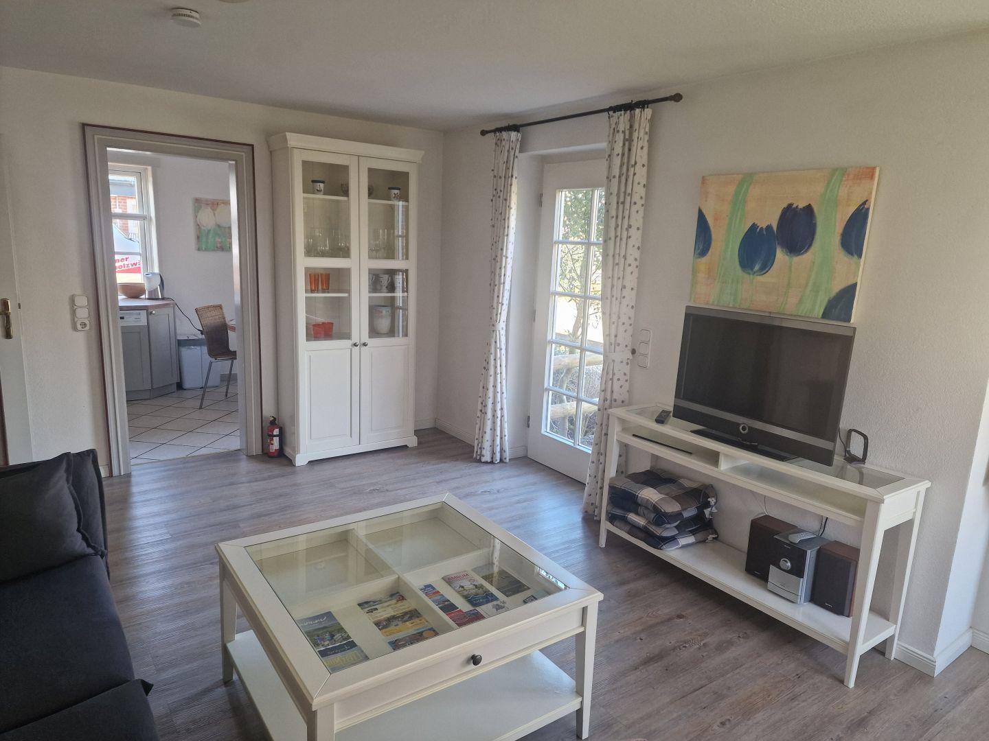 Wohnzimmer mit Fernseher, Glas-Tisch und weißen Möbeln.