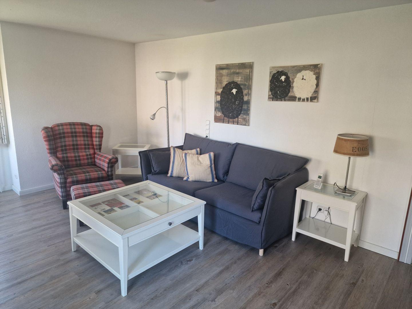 Wohnzimmer mit Sofa, Sessel, Tisch und Wandbildern.