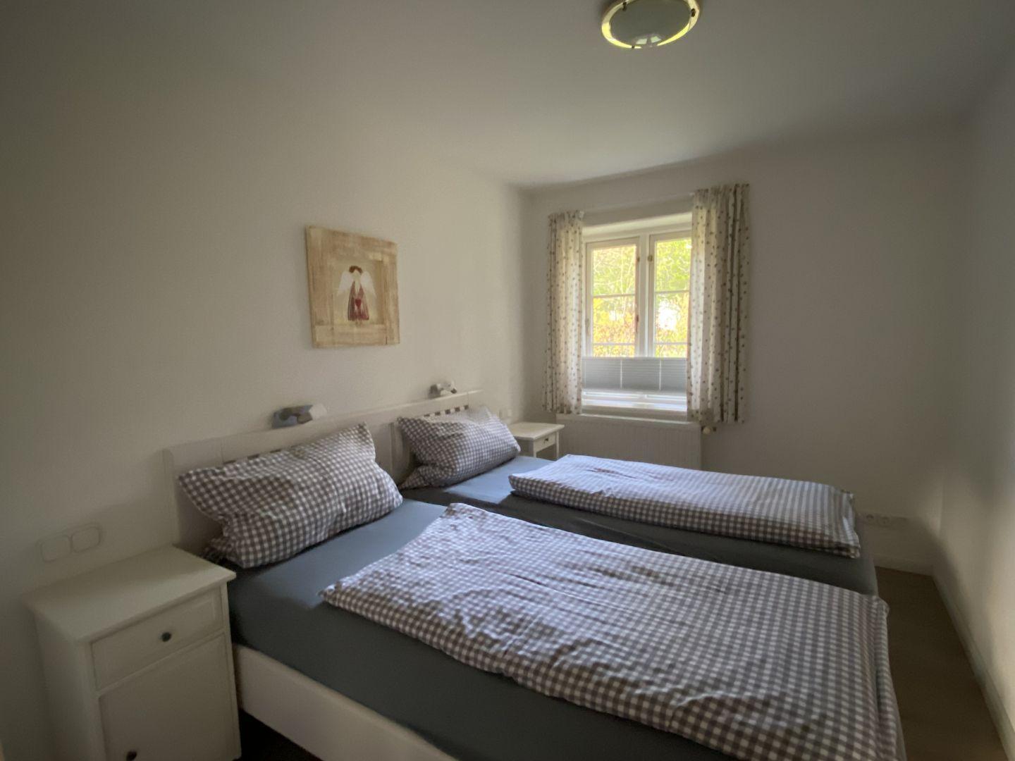Zwei Betten mit karierten Bettwäsche, Fenster mit Vorhängen, Nachttisch und Wandbild.