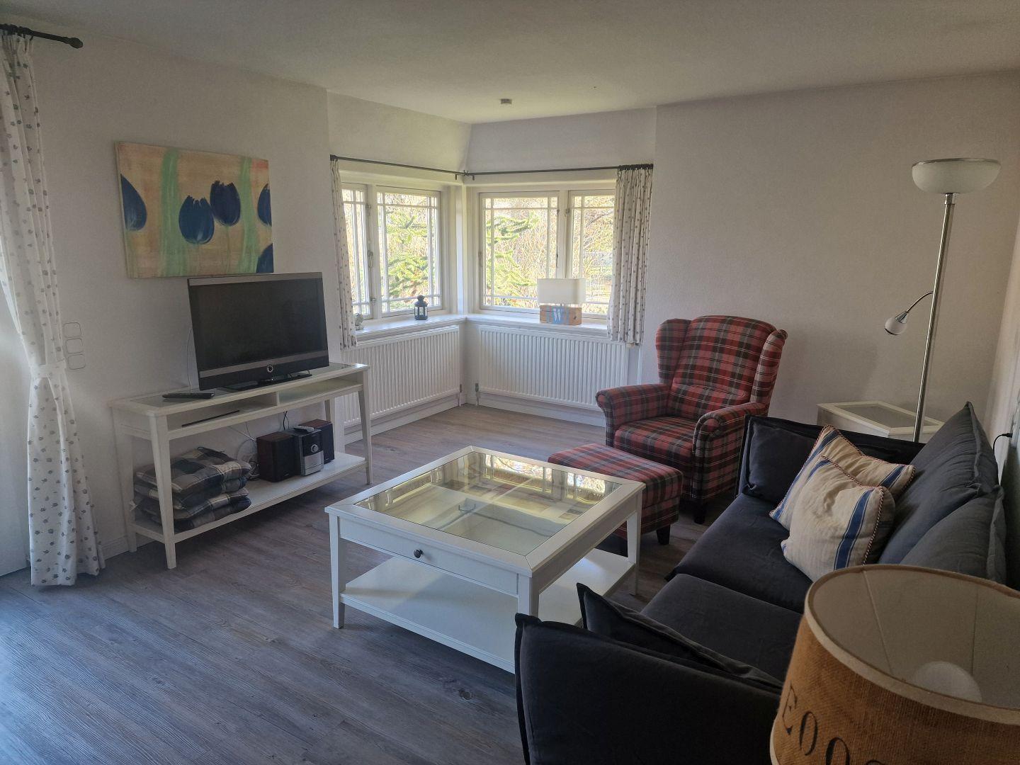 Wohnzimmer mit Sofa, Sessel, Fernseher und Fenster.