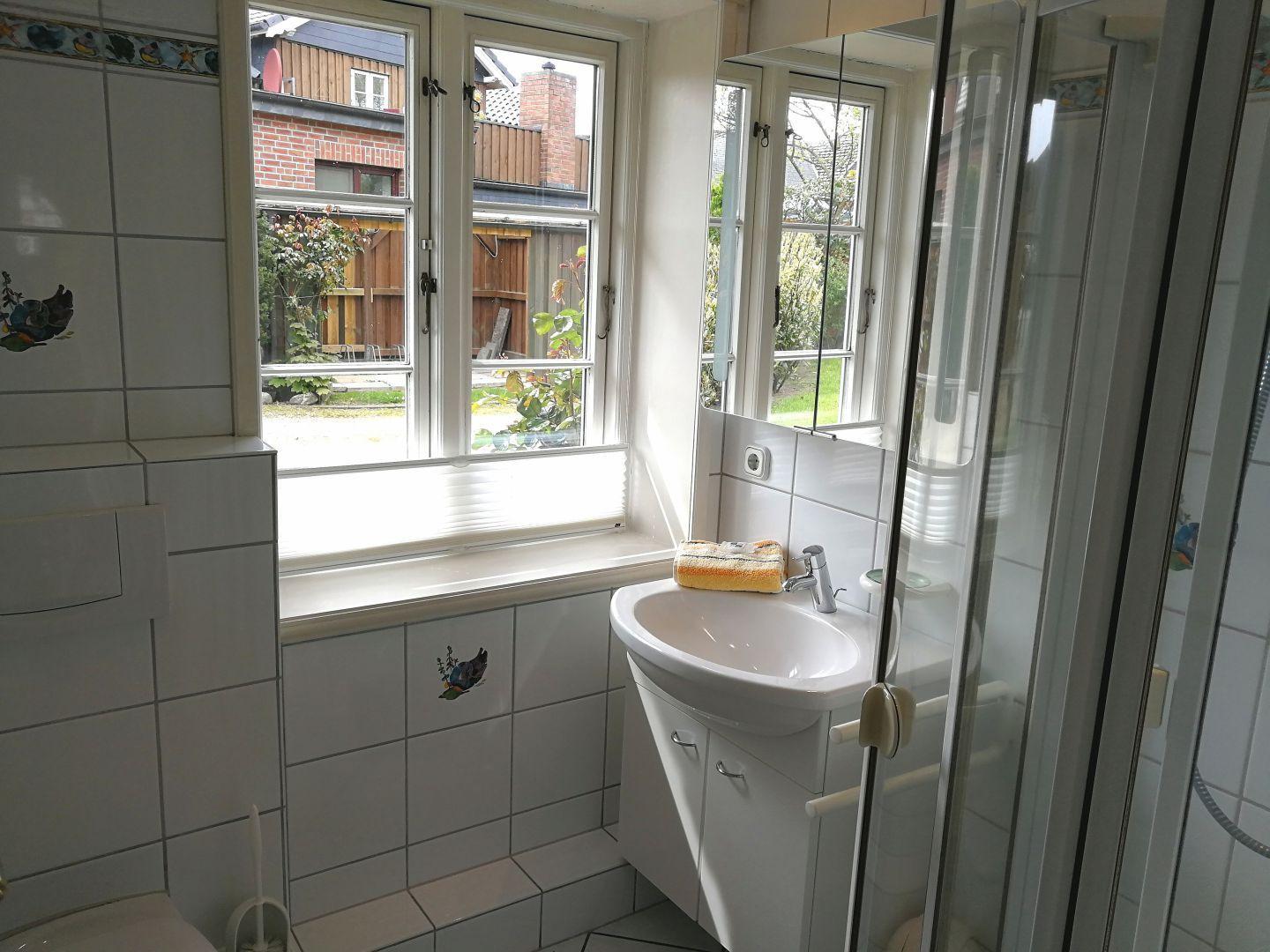 Badezimmer mit Waschbecken, Dusche und Fenster zur Außenseite.