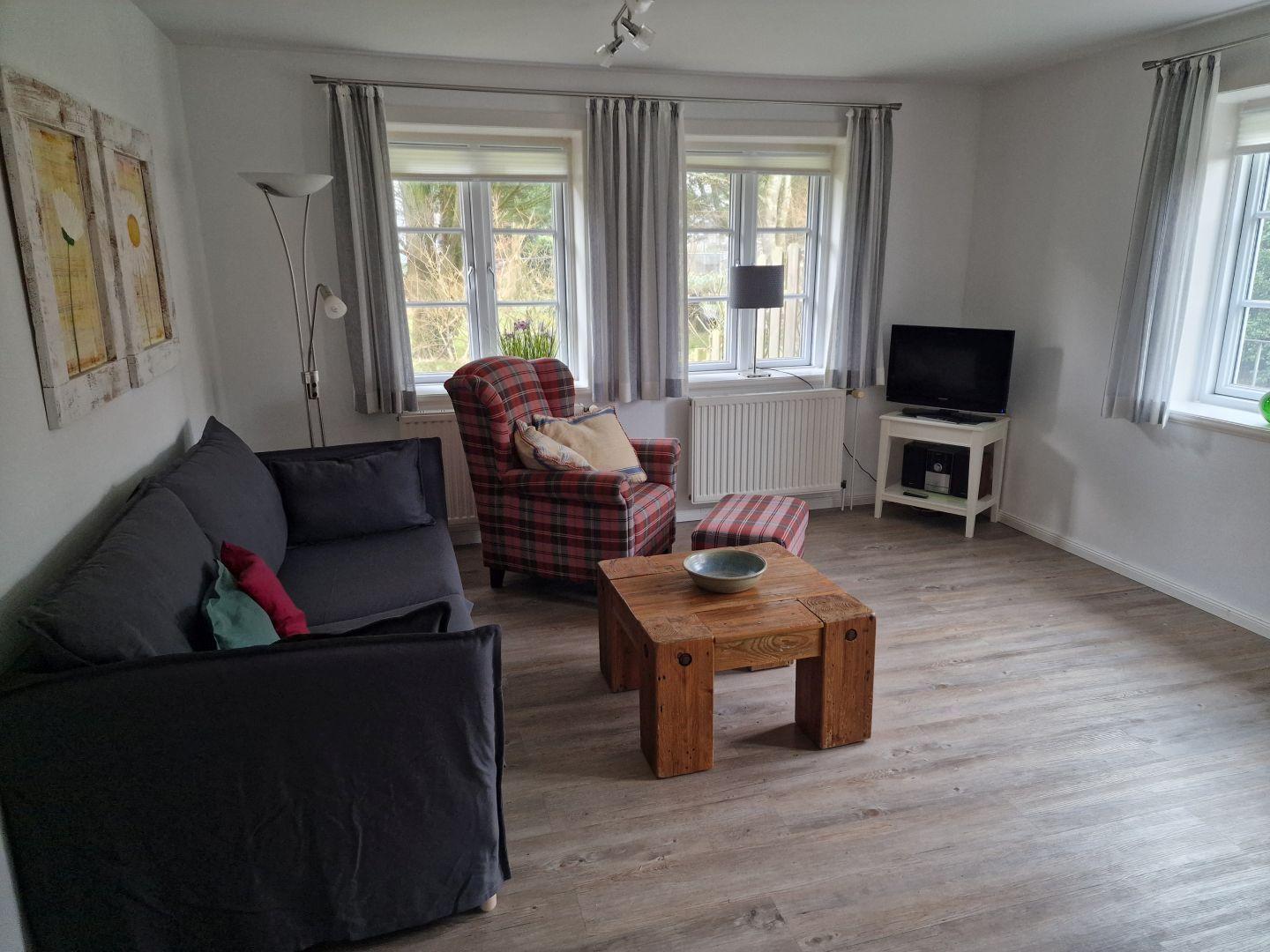 Wohnzimmer mit Sofa, Sessel, Tisch und Fernseher.