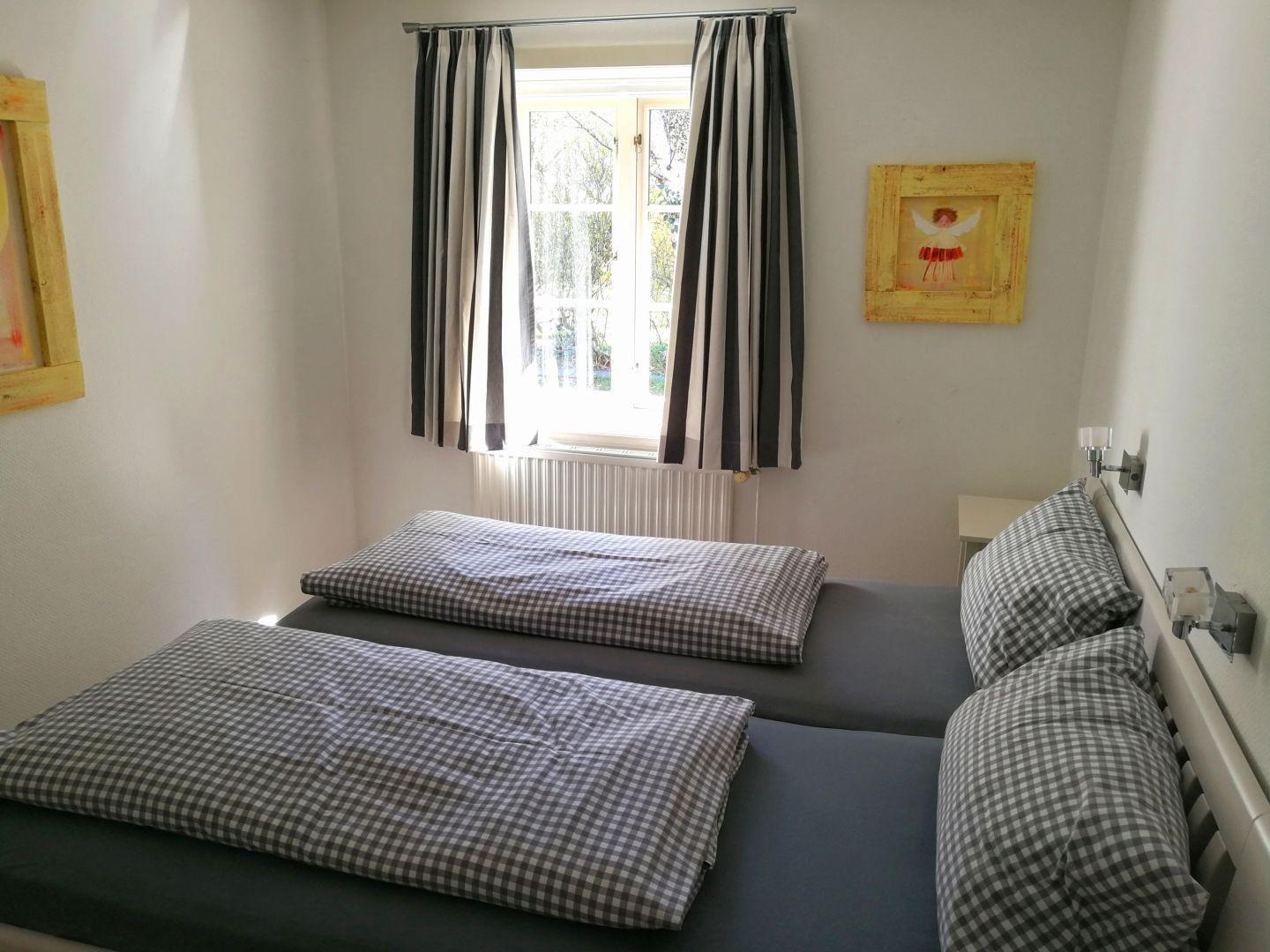 Zwei Betten mit karierten Bettwäsche, Fenster mit Streifenstoren und Wandbilder.