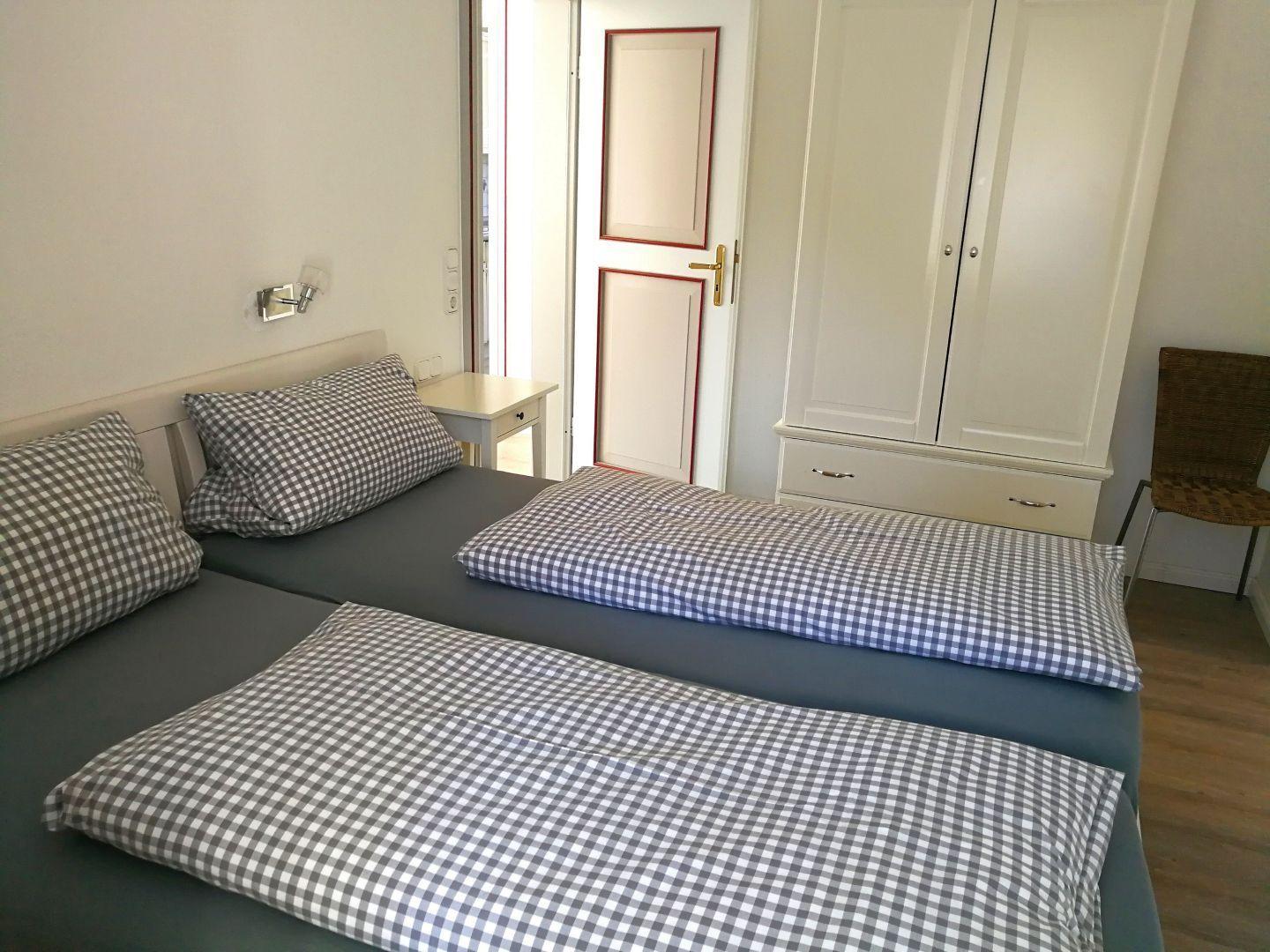 Zwei Betten mit karierten Bettwäsche, Schrank und Stuhl im Schlafzimmer.