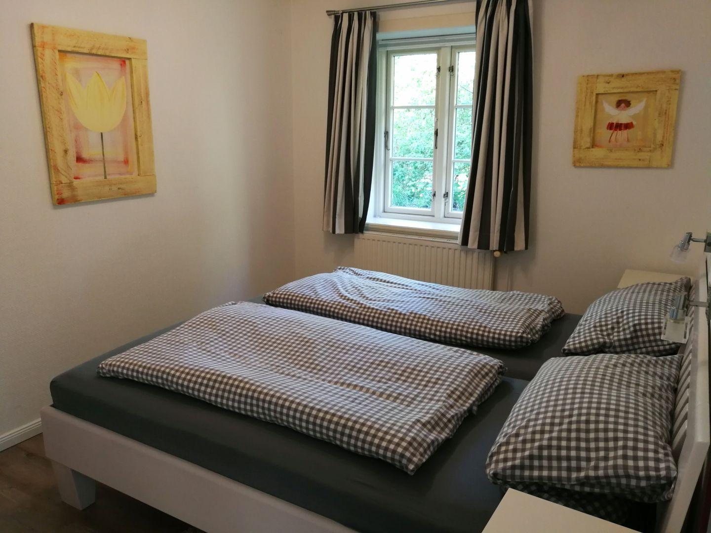 Schlafzimmer mit Doppelbett, Fenster und Wandbildern.