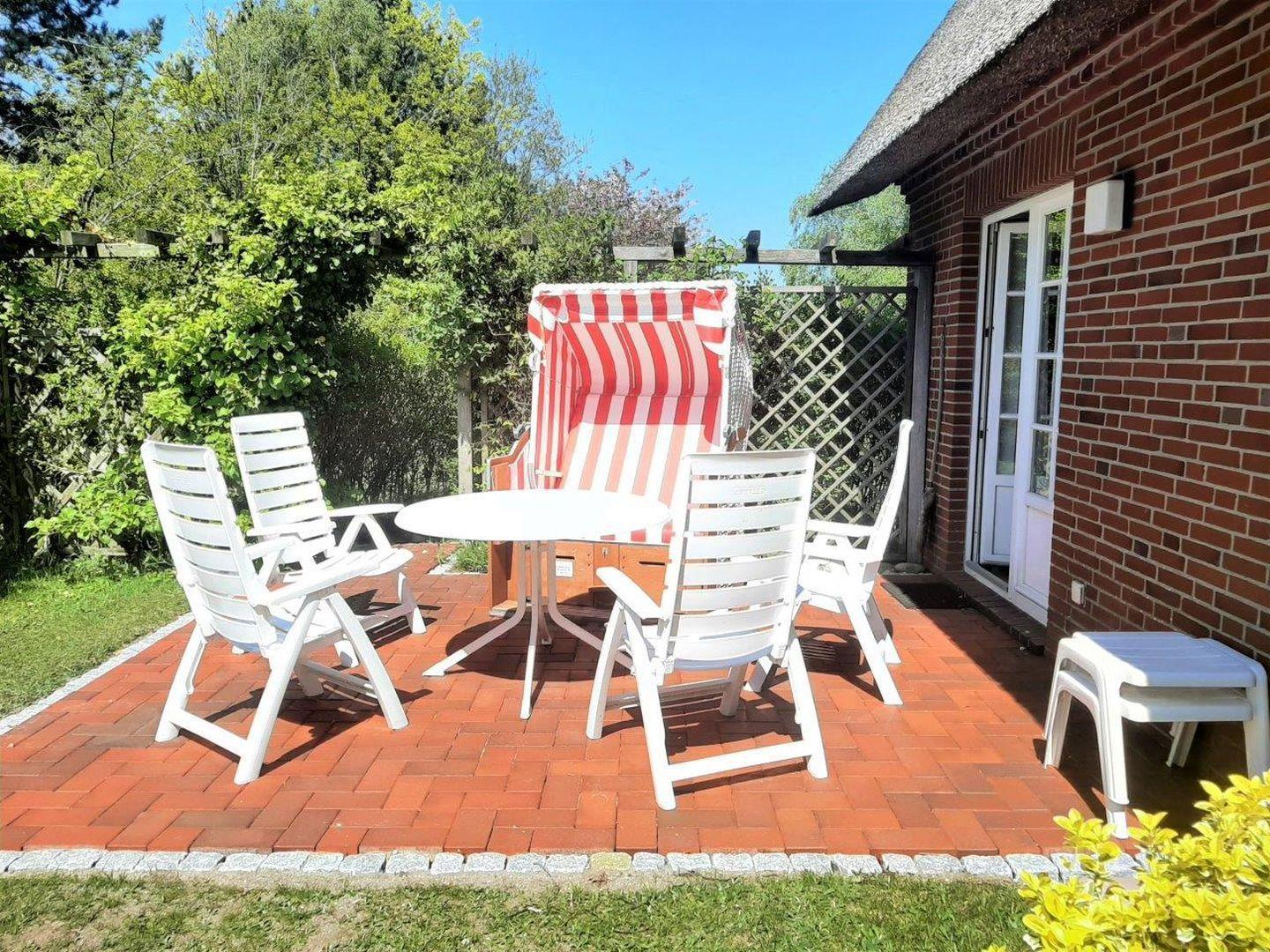 Terrasse mit weißem Tisch, vier Stühlen und einer rot-weißen Strandliege.