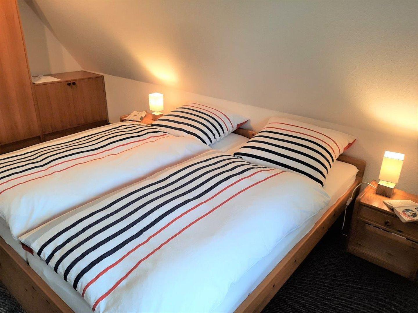 Schlafzimmer mit Doppelbett, zwei Nachttischen und Lampen. Holzmöbel und schräger Dachfirst.