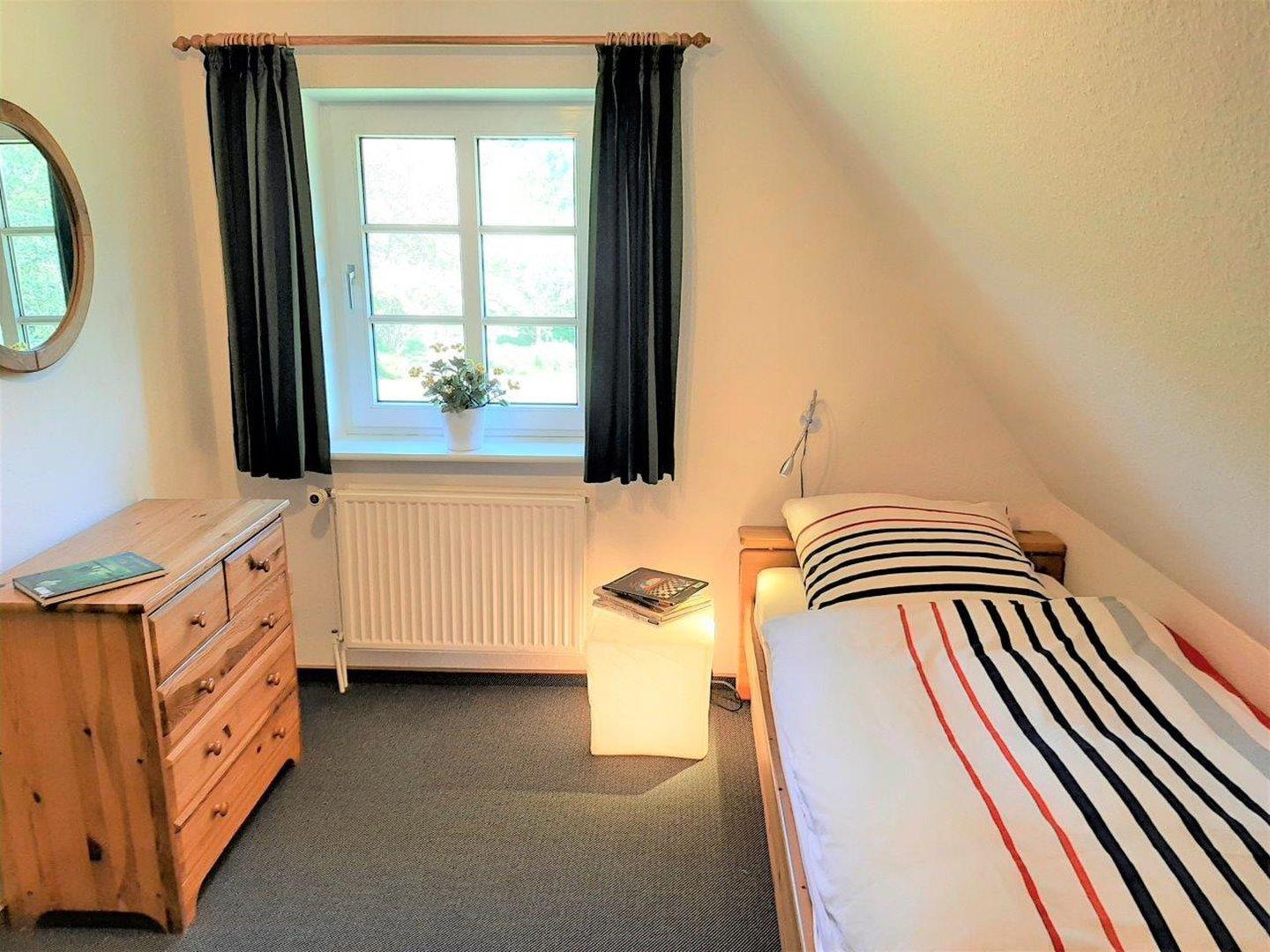 Ein Schlafzimmer mit Bett, Schrank und Fenster. Auf dem Fensterbrett steht eine Pflanze.
