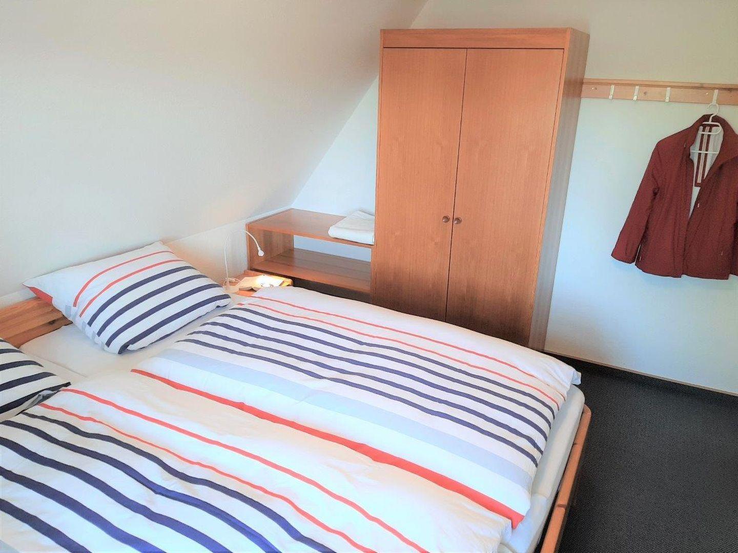 Schlafzimmer mit Bett, Kleiderschrank und Jacke an Wandhaken.