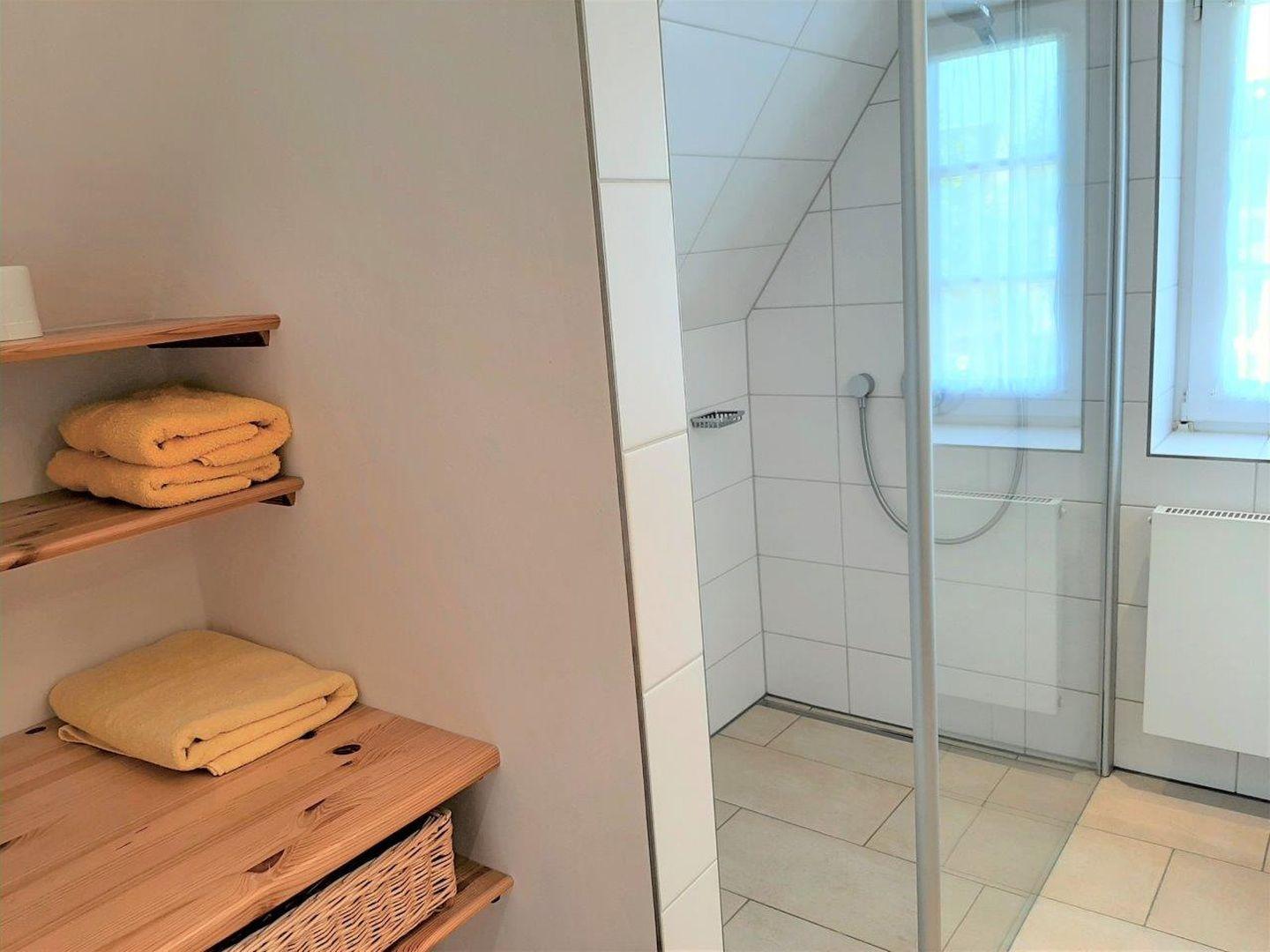 Bad mit Dusche, Holzregal und gelben Handtüchern.