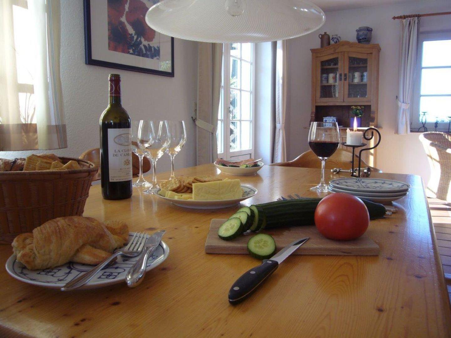 Holztisch mit Frühstück, Wein, Gemüse und Kerze.