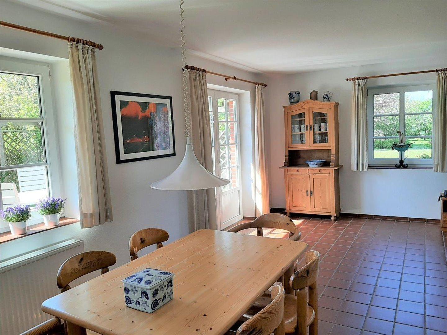 Esszimmer mit Holztisch, Stühlen und Terrassentür. Terrakottafußboden und Holzschrank.