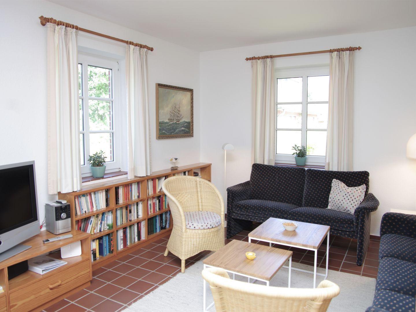 Wohnzimmer mit Sofa, Bücherregal, Fernseher und zwei Fenstern.