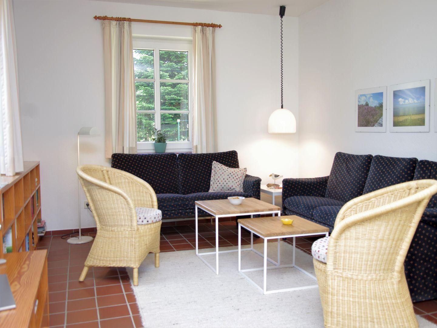 Wohnzimmer mit zwei Sofas, zwei Stühlen und einem Tisch. Fenster mit Vorhängen und Wandbilder.