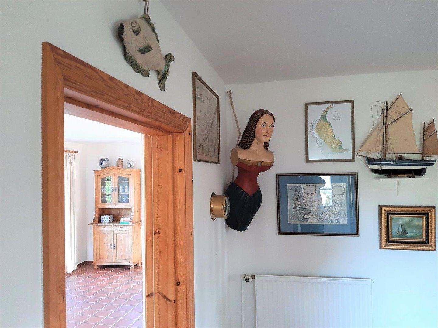 Eingangsbereich mit Holztür, Wanddekoration und Blick in Wohnzimmer mit Schrank.