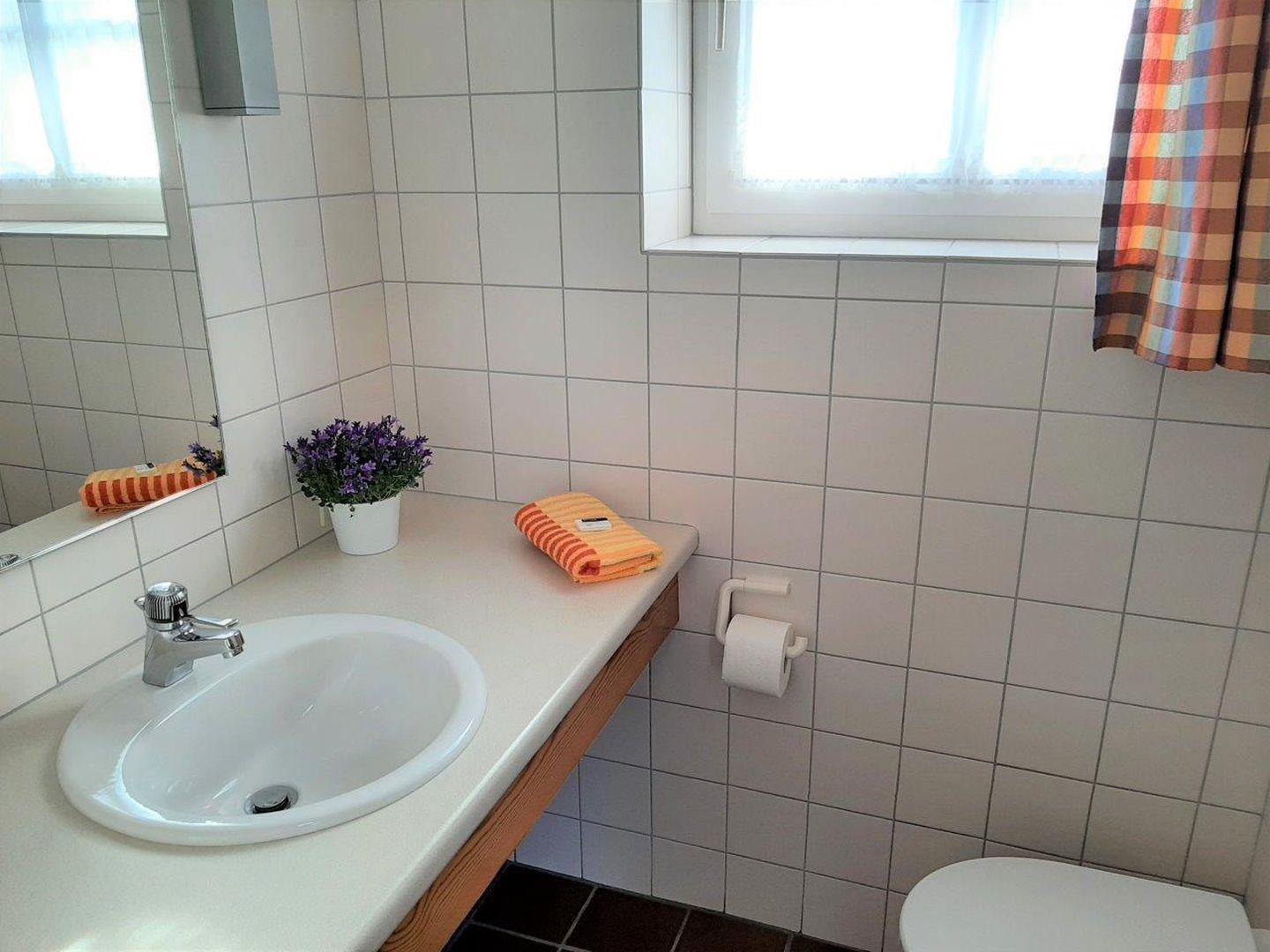 Badezimmer mit Waschbecken, Spiegel, Toilette und Fenster.
