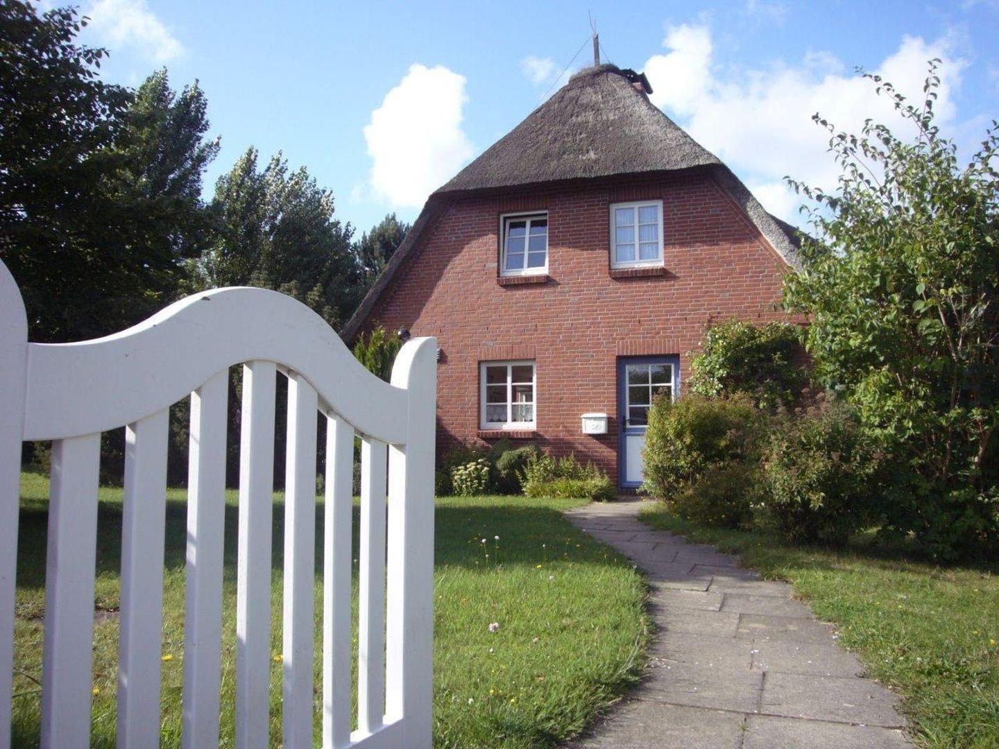 Rotes Backsteingebäude mit Strohdach, weißer Torbogen und gepflasterter Weg.