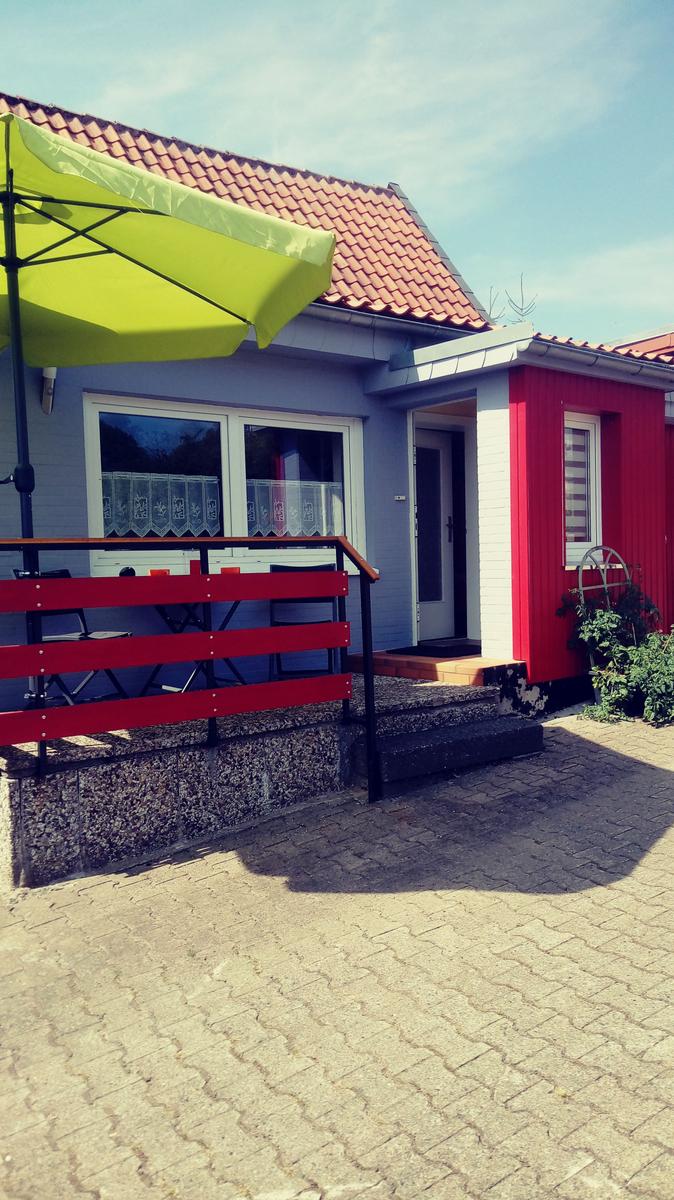 Rot-weißes Haus mit Terrasse, grüner Sonnenschirm und roter Bank.