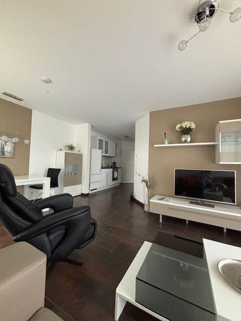 Living and dining area with kitchen, TV, and black leather chair.