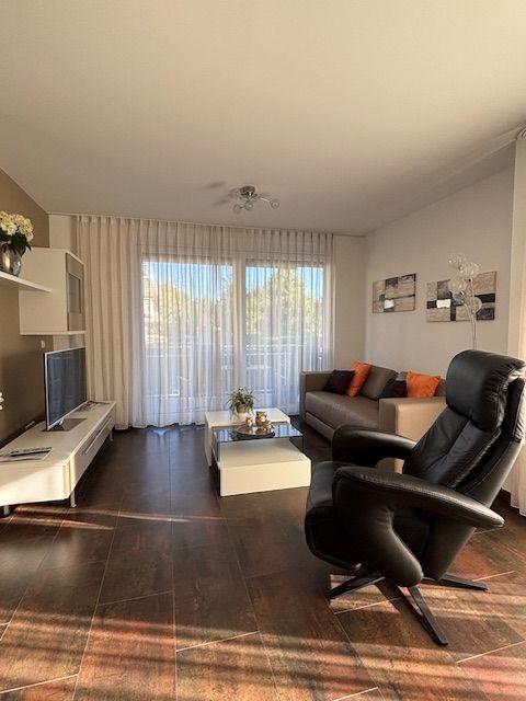 Living room with sofa, leather chair, TV, and window with curtains.