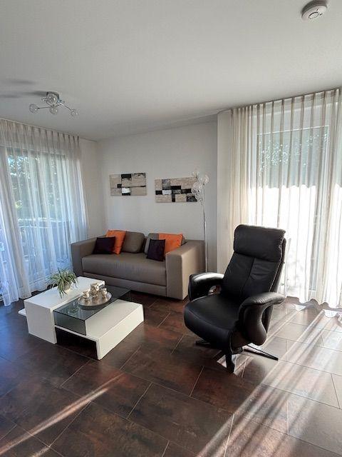 Living room with sofa, chair, and glass table near large windows.