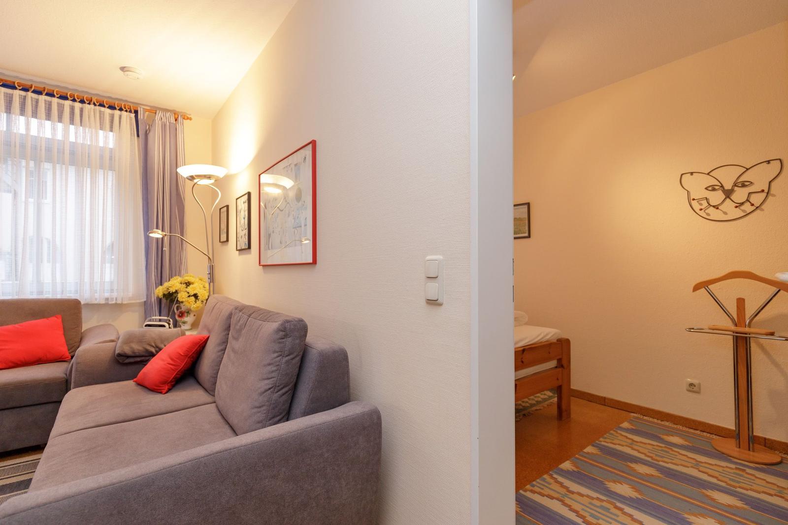 Wohnbereich mit Sofa und Schlafzimmer mit Bett und Kleiderständer