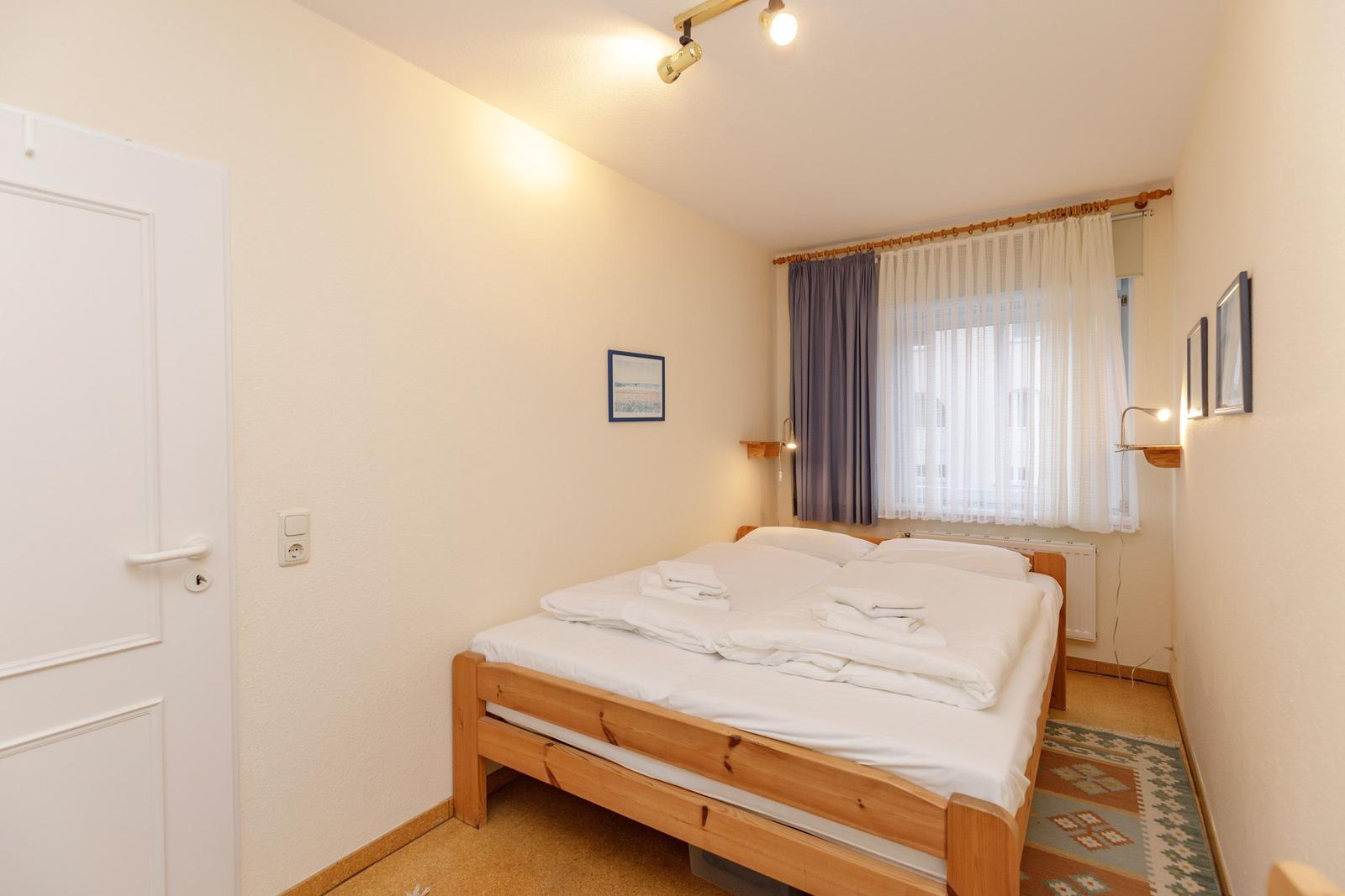 Schlafzimmer mit Holzbett, Fenster und Tür.