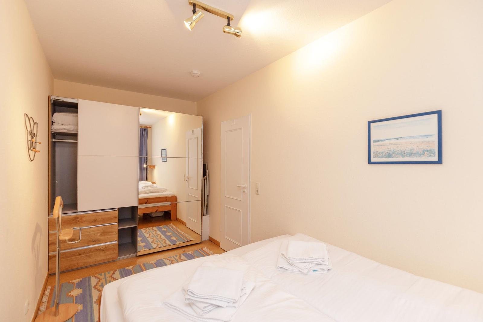 Schlafzimmer mit Bett, Kleiderschrank und Spiegel. Deckenleuchte und Wandbild.