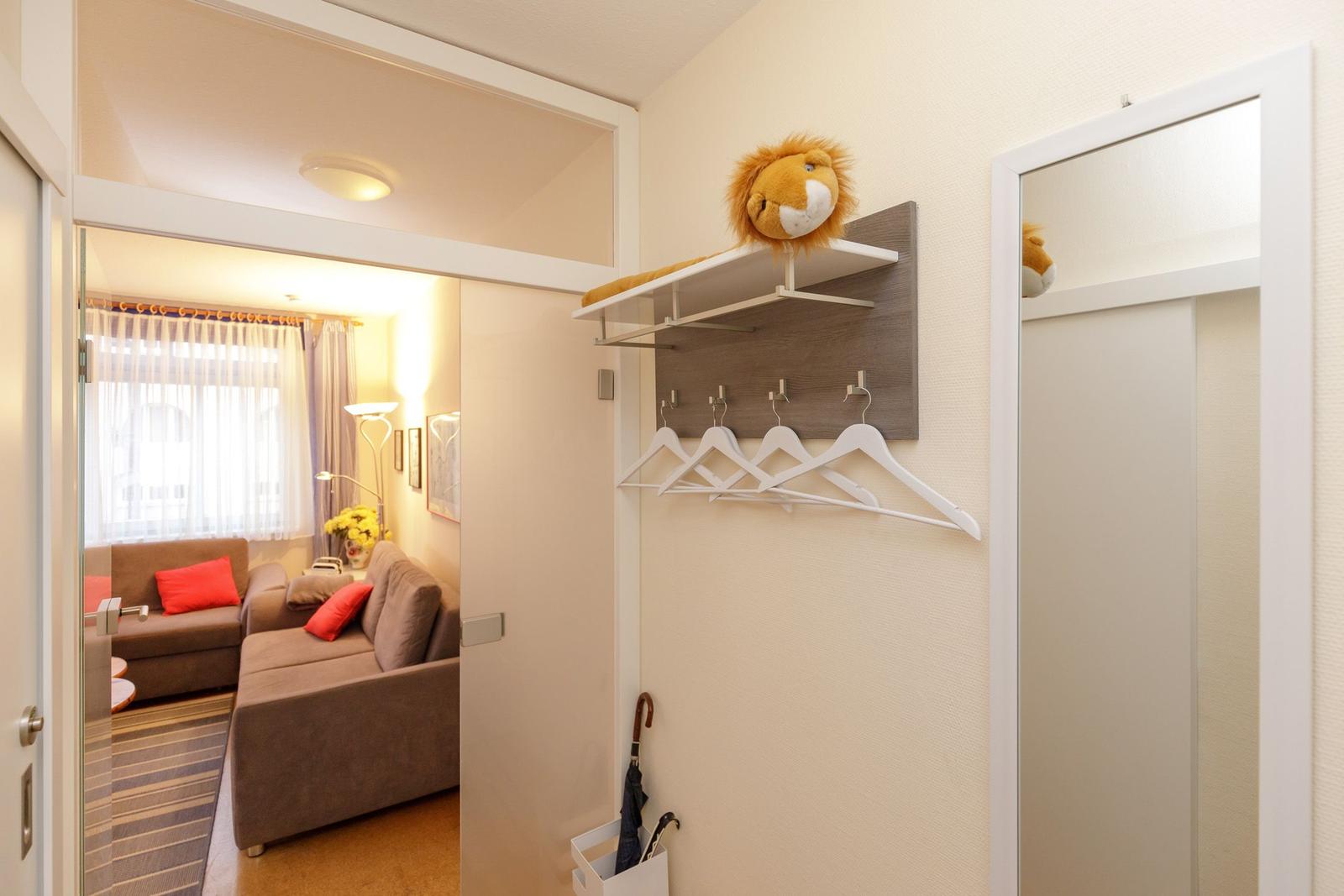 Eingangsbereich mit Garderobe, Spiegel und Sicht auf Wohnzimmer mit Sofa.