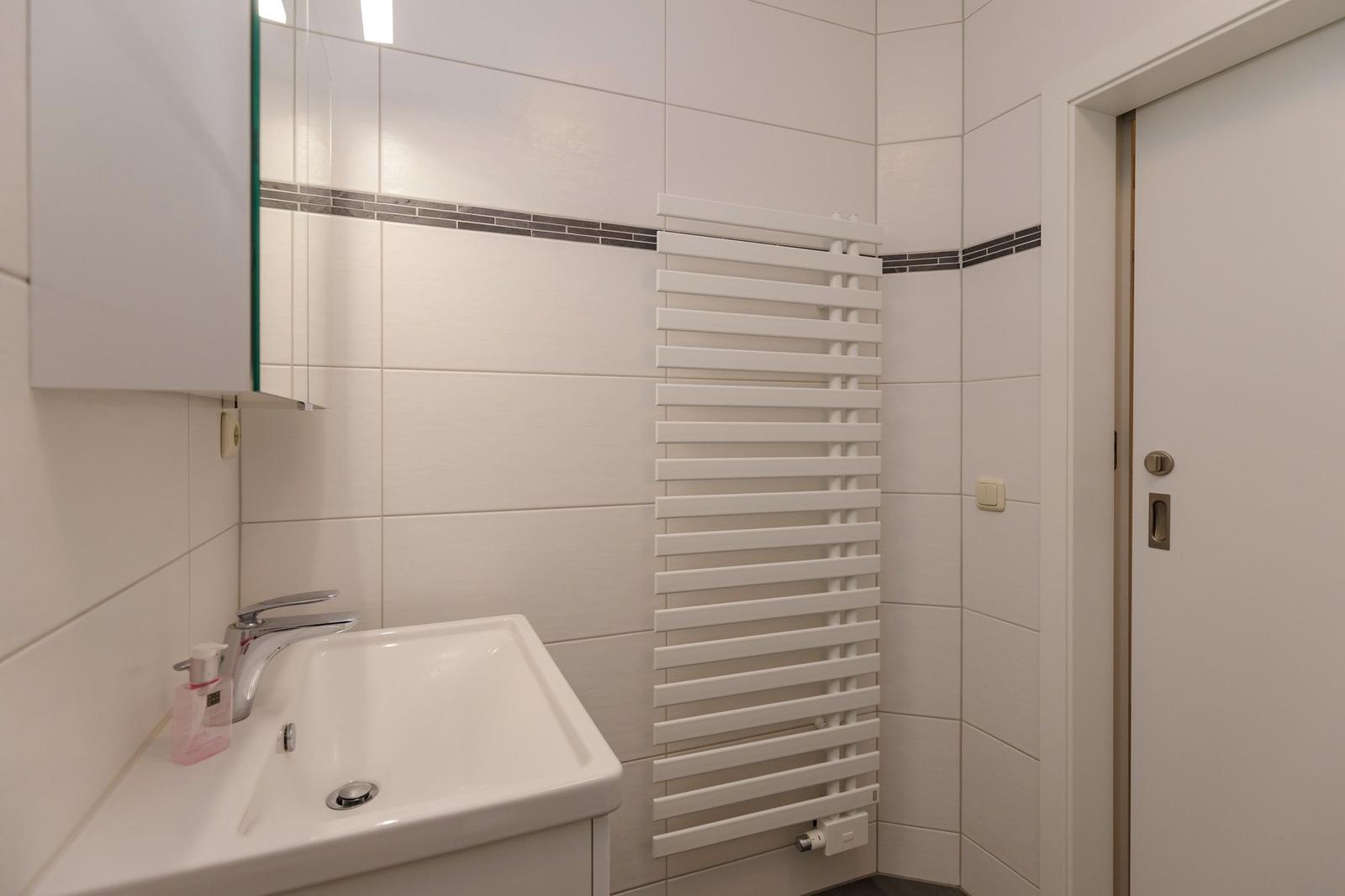 Badezimmer mit Waschbecken, Spiegelschrank und Heizkörper.