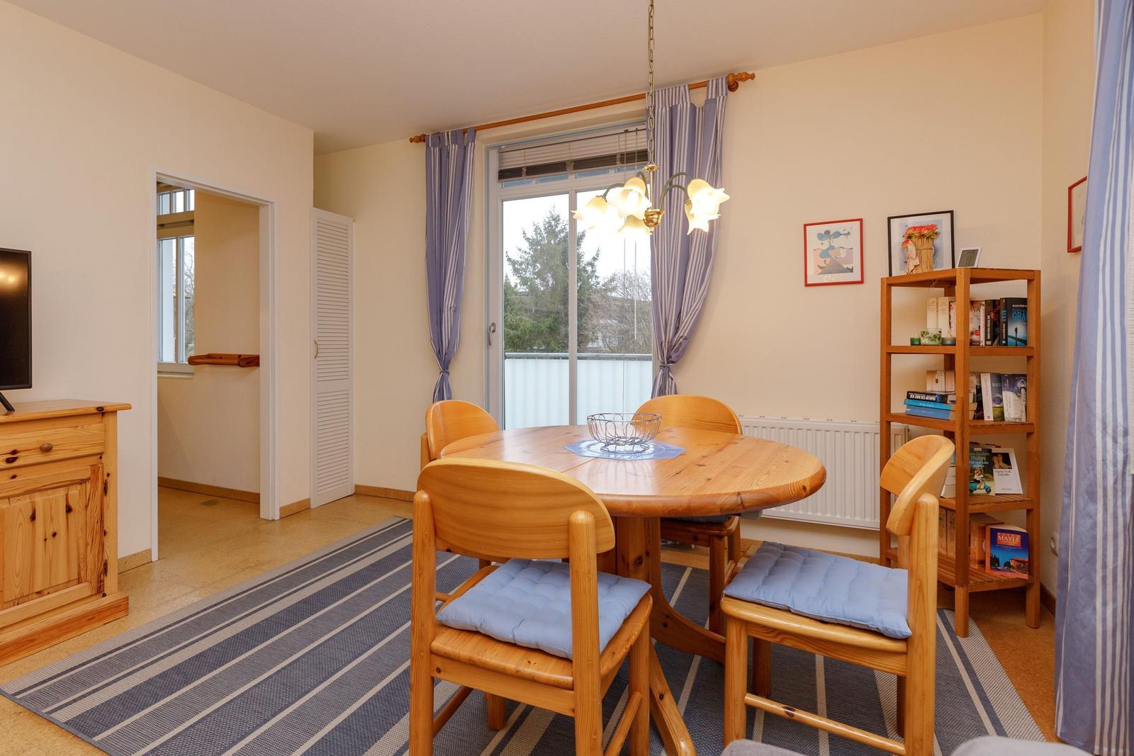 Esszimmer mit Holztisch, Stühlen und Balkontür. Bücherregal und TV-Schrank sichtbar.