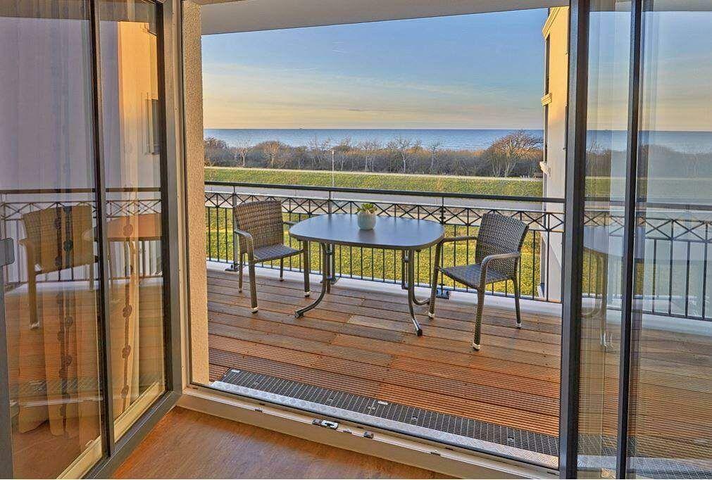 Terrasse mit Tisch und Stühlen, Blick auf Meer und Wiese.