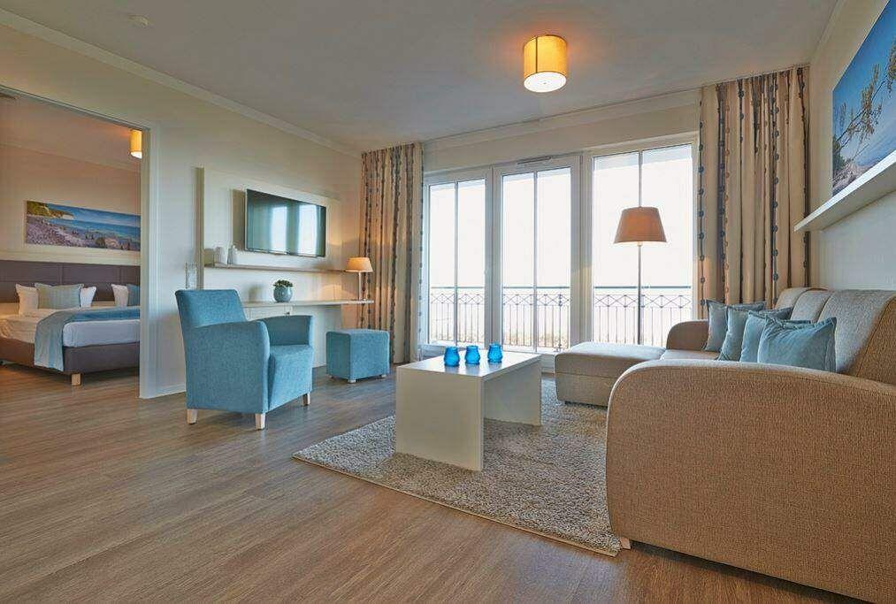 Wohnzimmer mit Sofa, Sessel und Balkon. Schlafzimmer im Hintergrund.