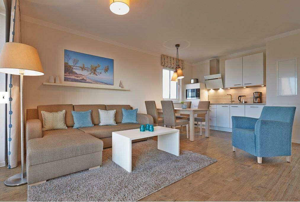 Wohnbereich mit Sofa, Couchtisch und Essbereich. Küche mit weißen Schränken.