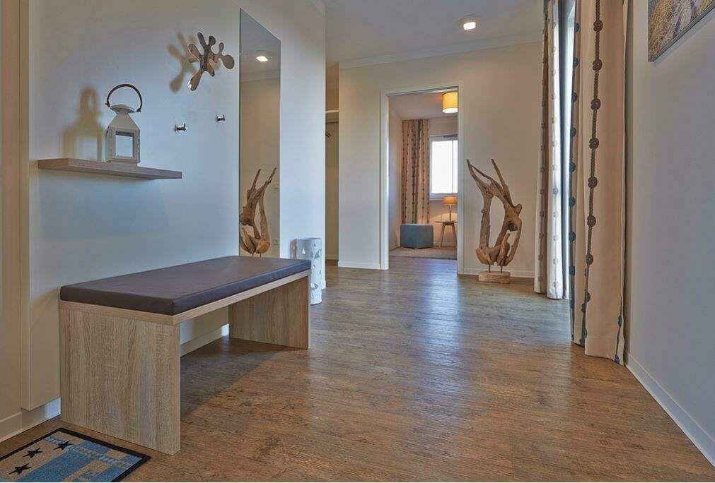 Helle Eingangshalle mit Holzboden und Sitzbank. Dekorative Holzobjekte und Spiegel sind sichtbar.