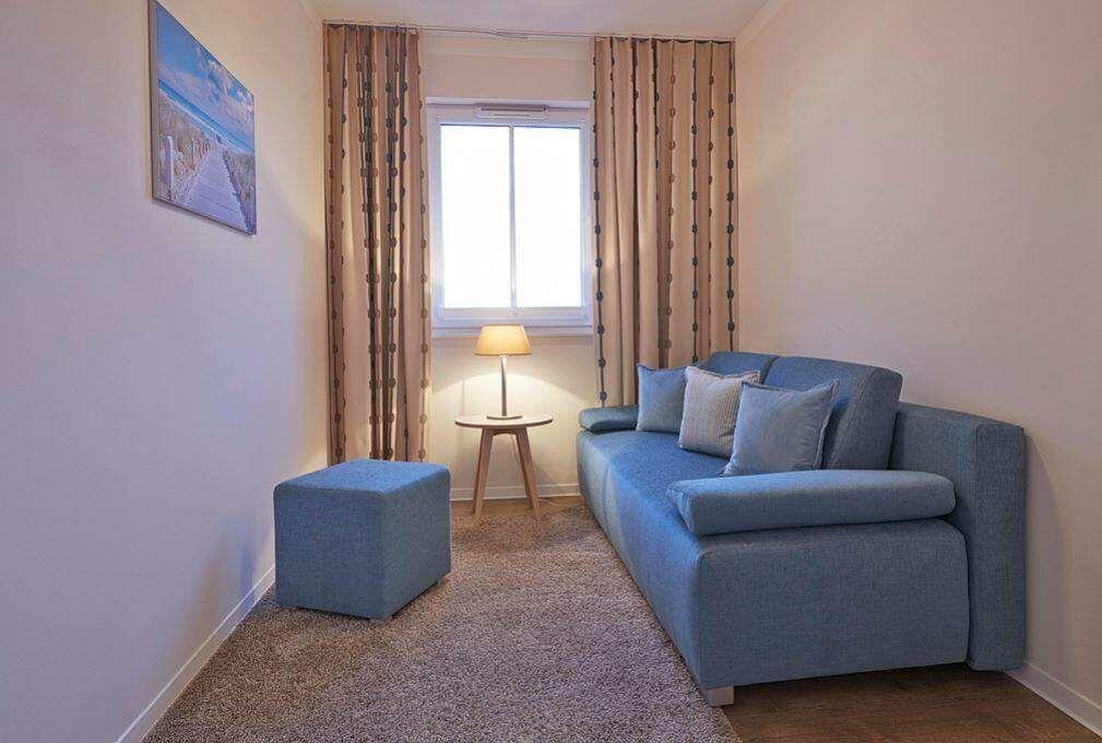 Ein Wohnzimmer mit blauem Sofa, Beistelltisch und Fenster mit Vorhängen.