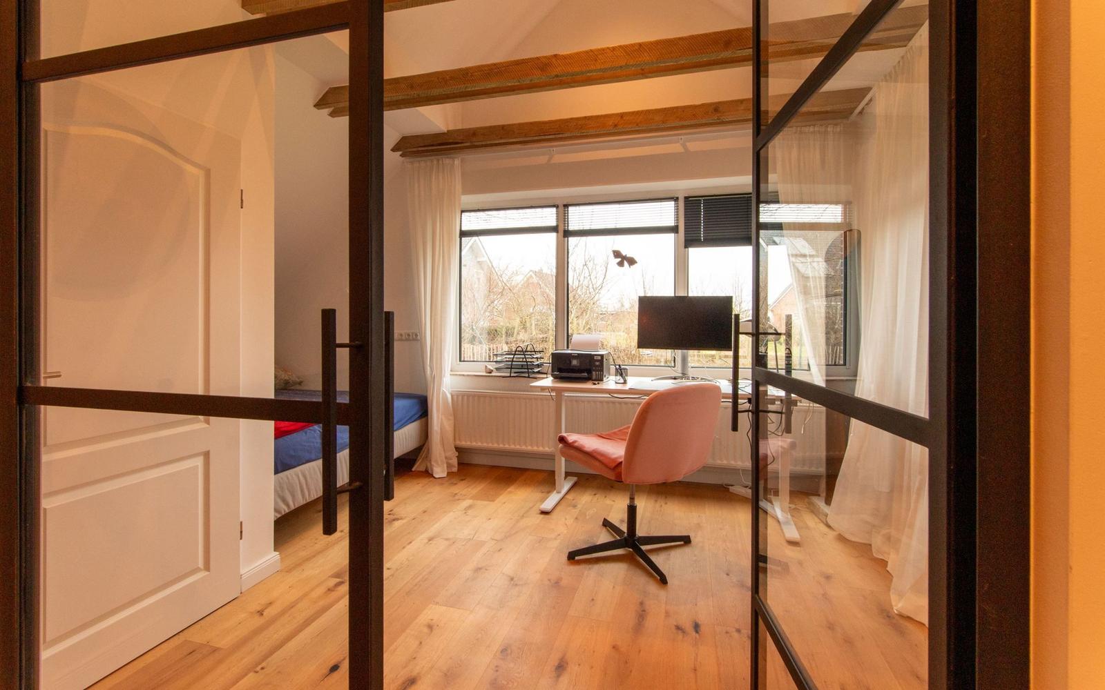 Ein Zimmer mit Schreibtisch, Stuhl und Bett hinter Glasschiebetür.