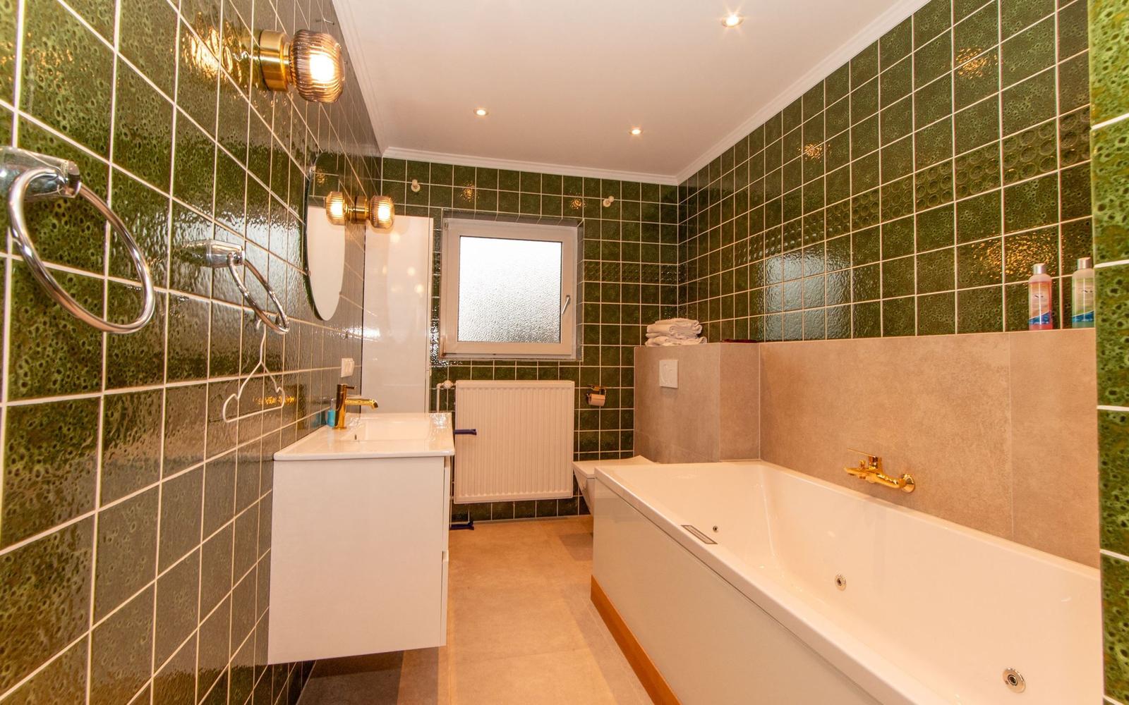 Badezimmer mit grünen Fliesen, Badewanne und Waschbecken.