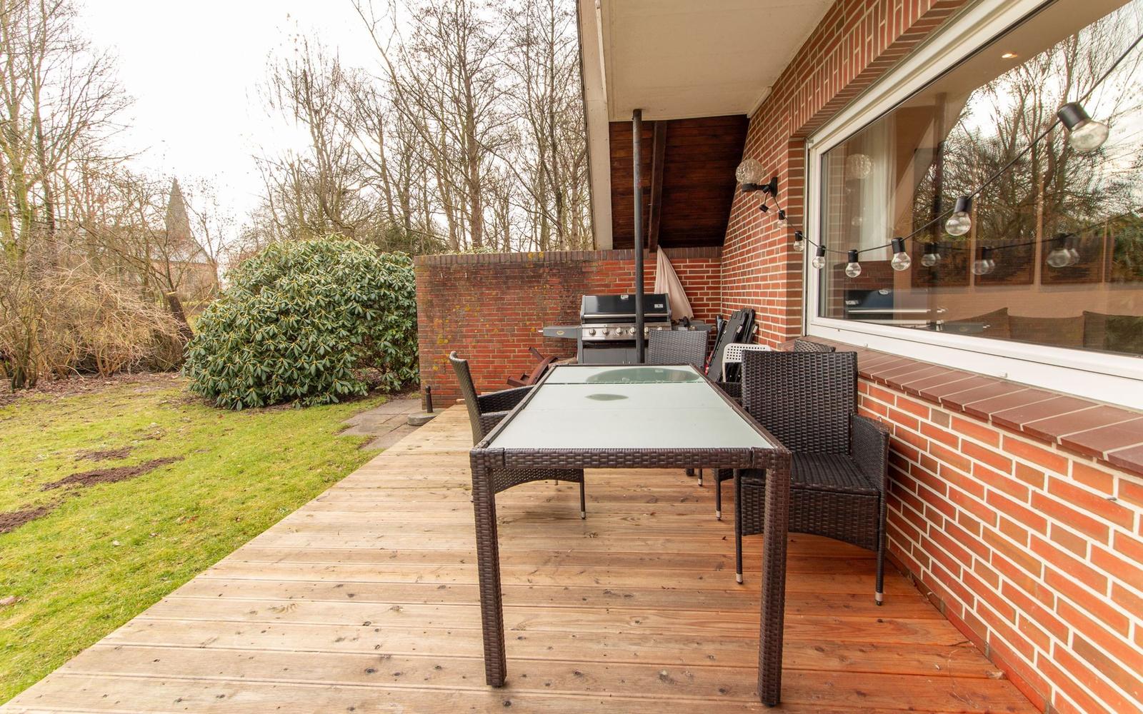 Terrasse mit Tisch, Stühlen und Grill. Holzdecke, Ziegelwand und Garten.